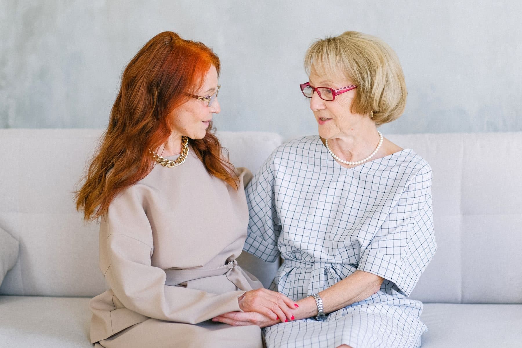 A carer holding hands with an older woman on a sofa