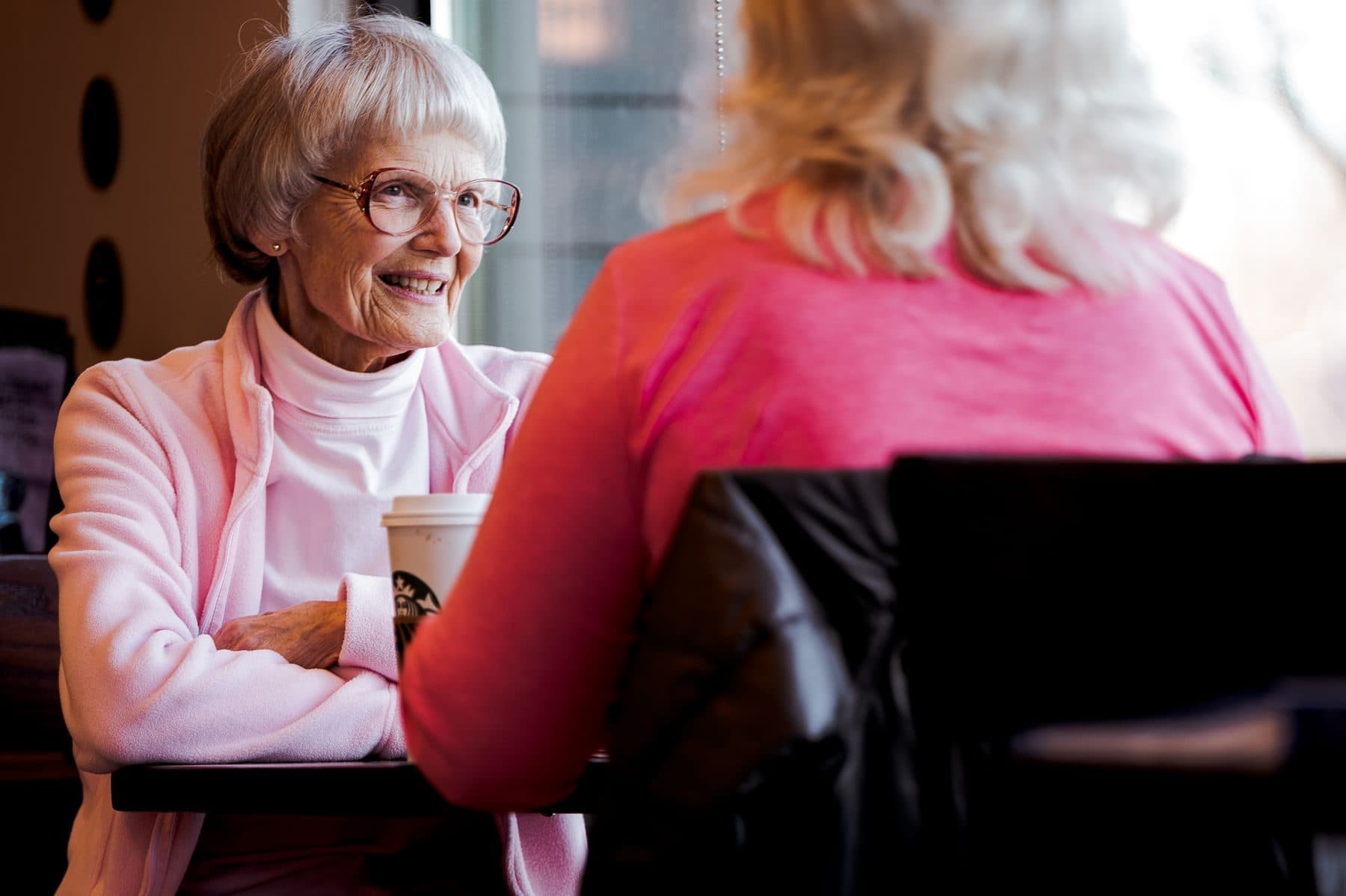 An older woman smiling while chatting with a carer over a cup of tea