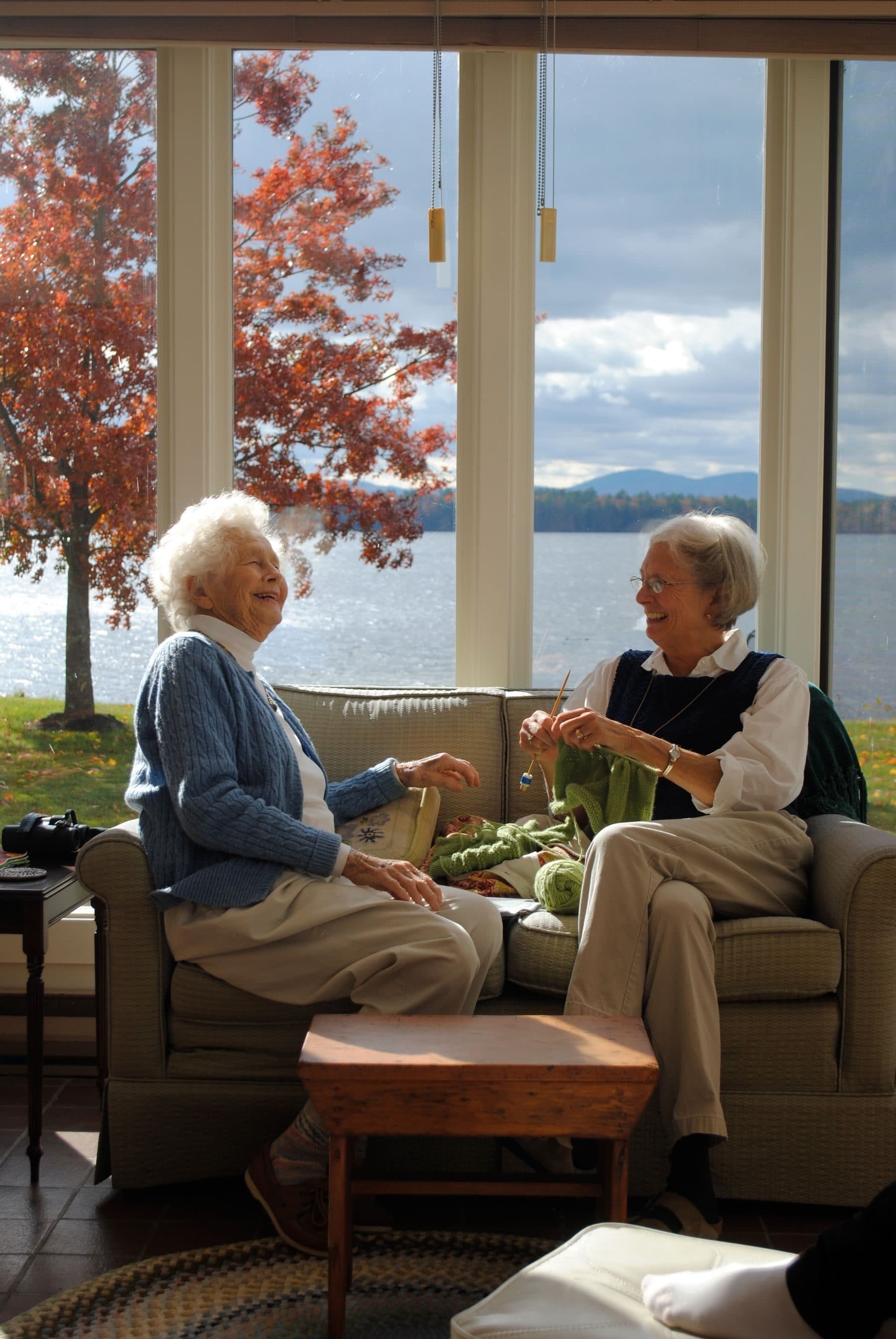Two older women laughing together in a bright living room