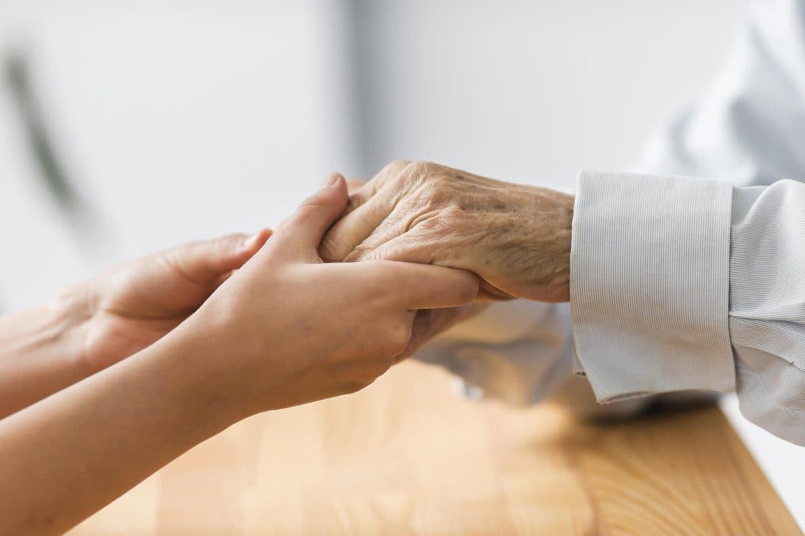 A carer gently holding the hands of an older man