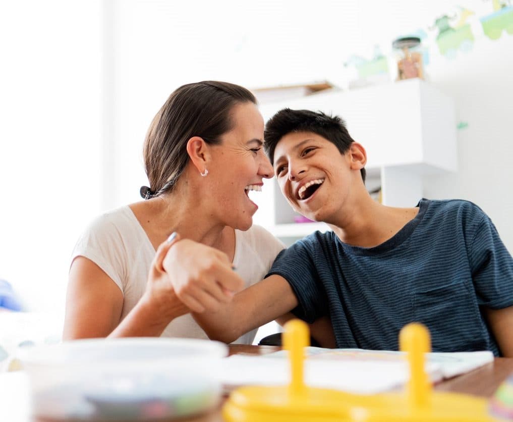 A support worker and a young man laughing together during an activity